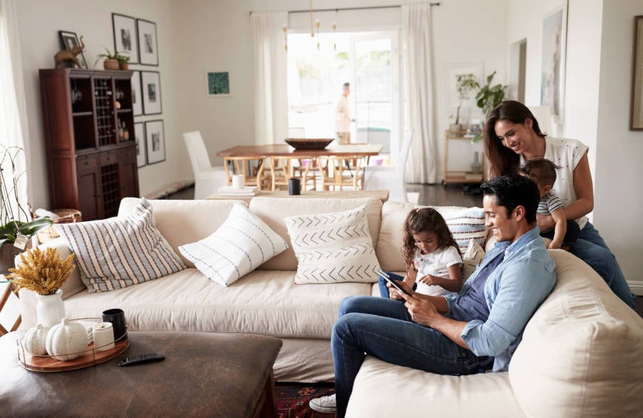 Family sitting on a sectional in living room, engaging with tablet.