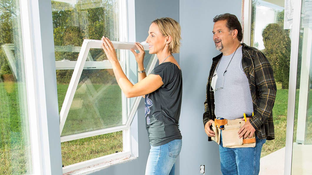 Woman opening new double hung windows as  home contractor watches.